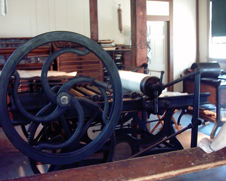 Another press
One person turns the wheel while the other feeds the paper and pulls it through and hangs it to dry. They printed local news mostly, on one side, but one day a month they would get the national news and print that on the other side to keep a well informed citizenry.

