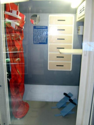 Cramped quarters
In space sleeping standing up is no different then laying down. The bag and foot holders keep astronauts from floating around. They have 3 quarters. A fourth person can sleep where he wants provided he is anchored to not float around.
